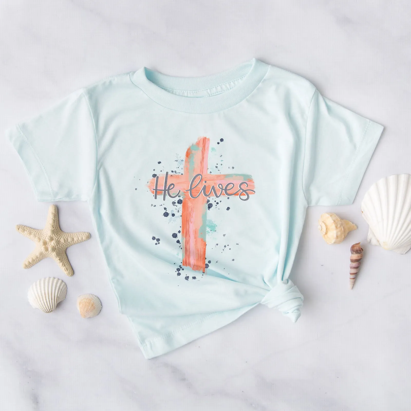 He lives Watercolor Cross Tee sold by Faithful and Co.